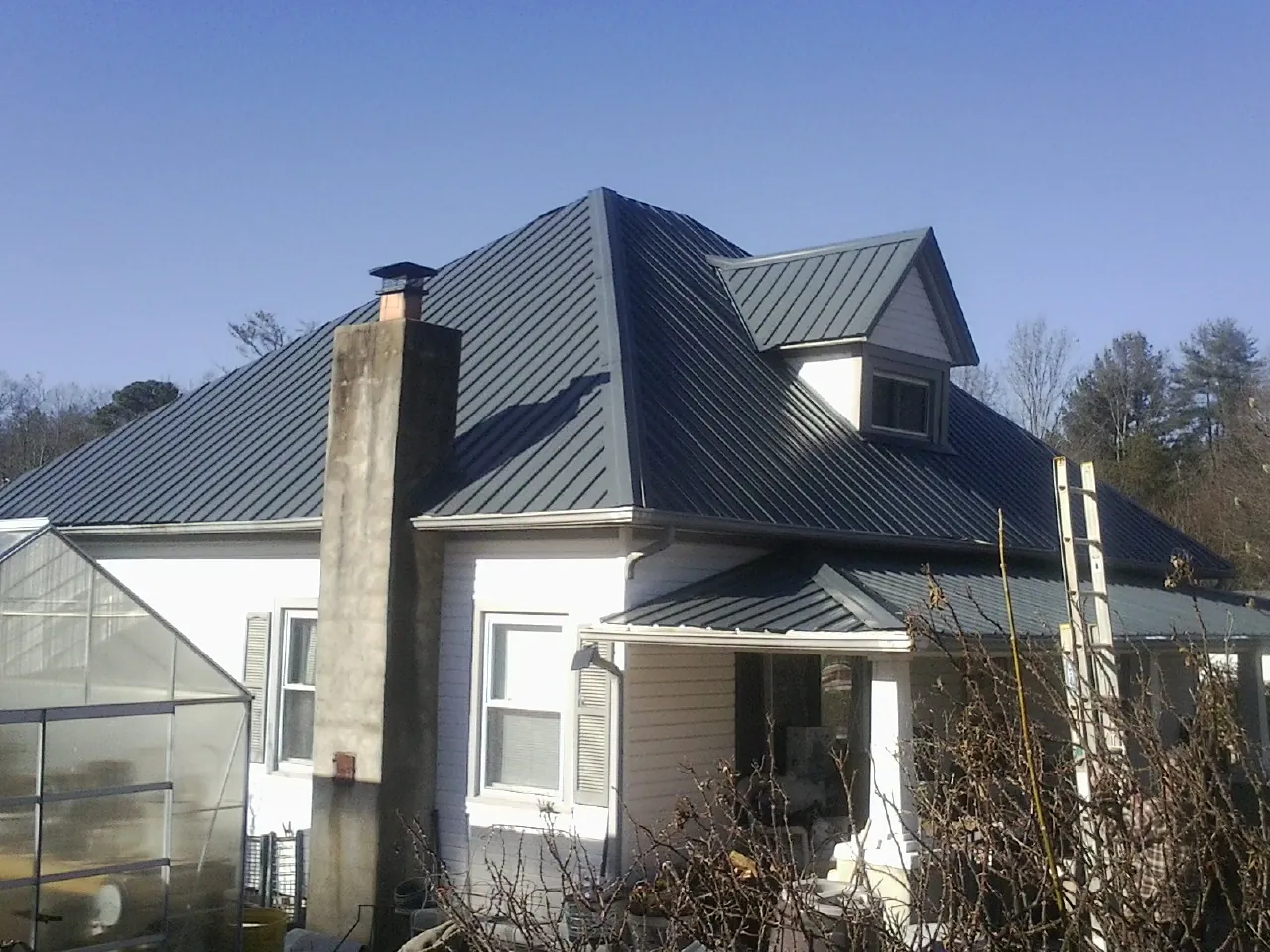 Dark blue standing seam metal roof on a white farmhouse with dormer — Slate & Tile Roof Repair by Roofing Brothers in Ovid