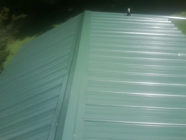 New green metal panels meeting at the ridge of a roof — Flat Roof Repair work by our crew in Ovid