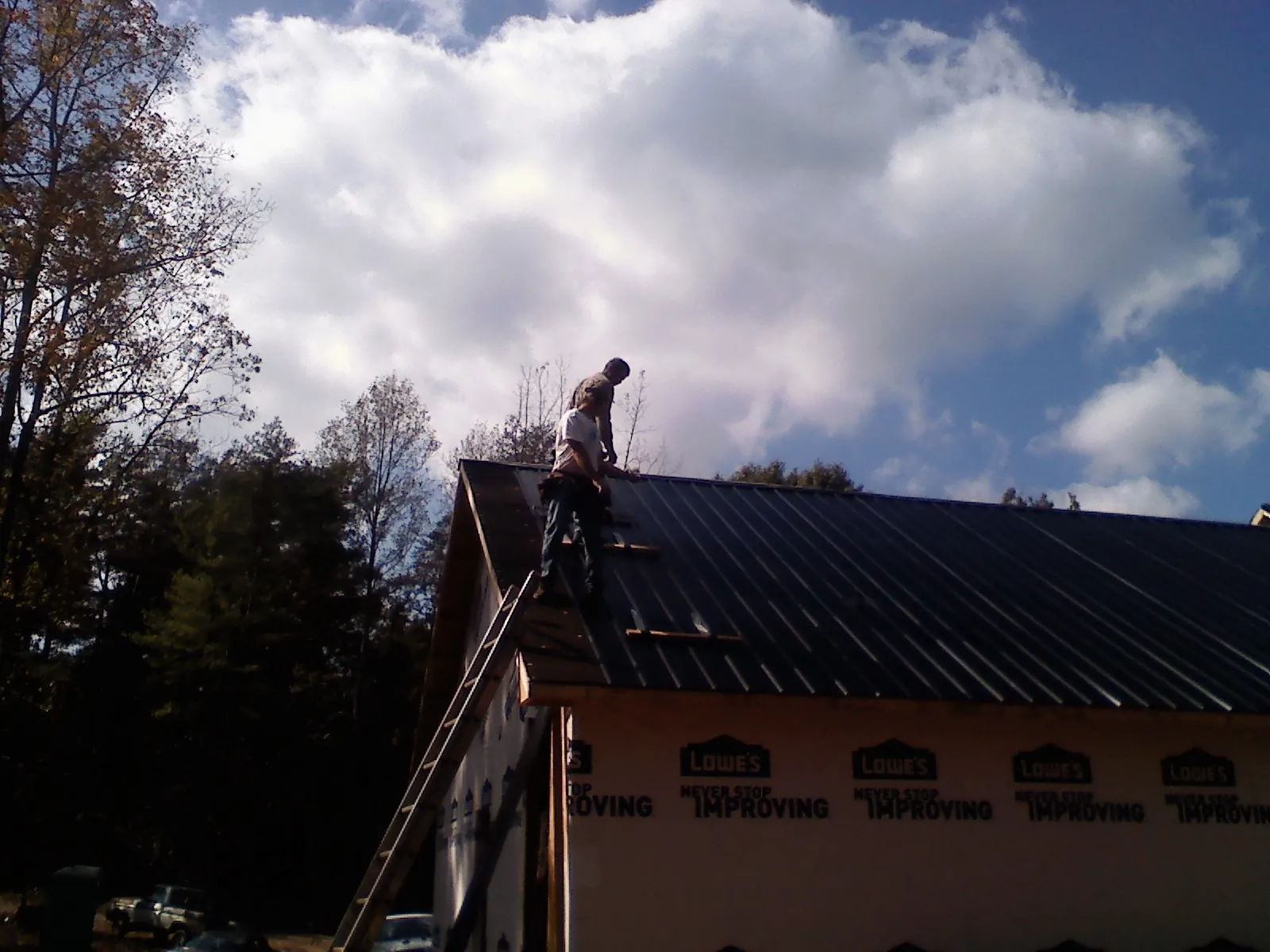 Roofer fastening dark metal panels high against a cloudy sky, from a Roof Inspection job in Ovid