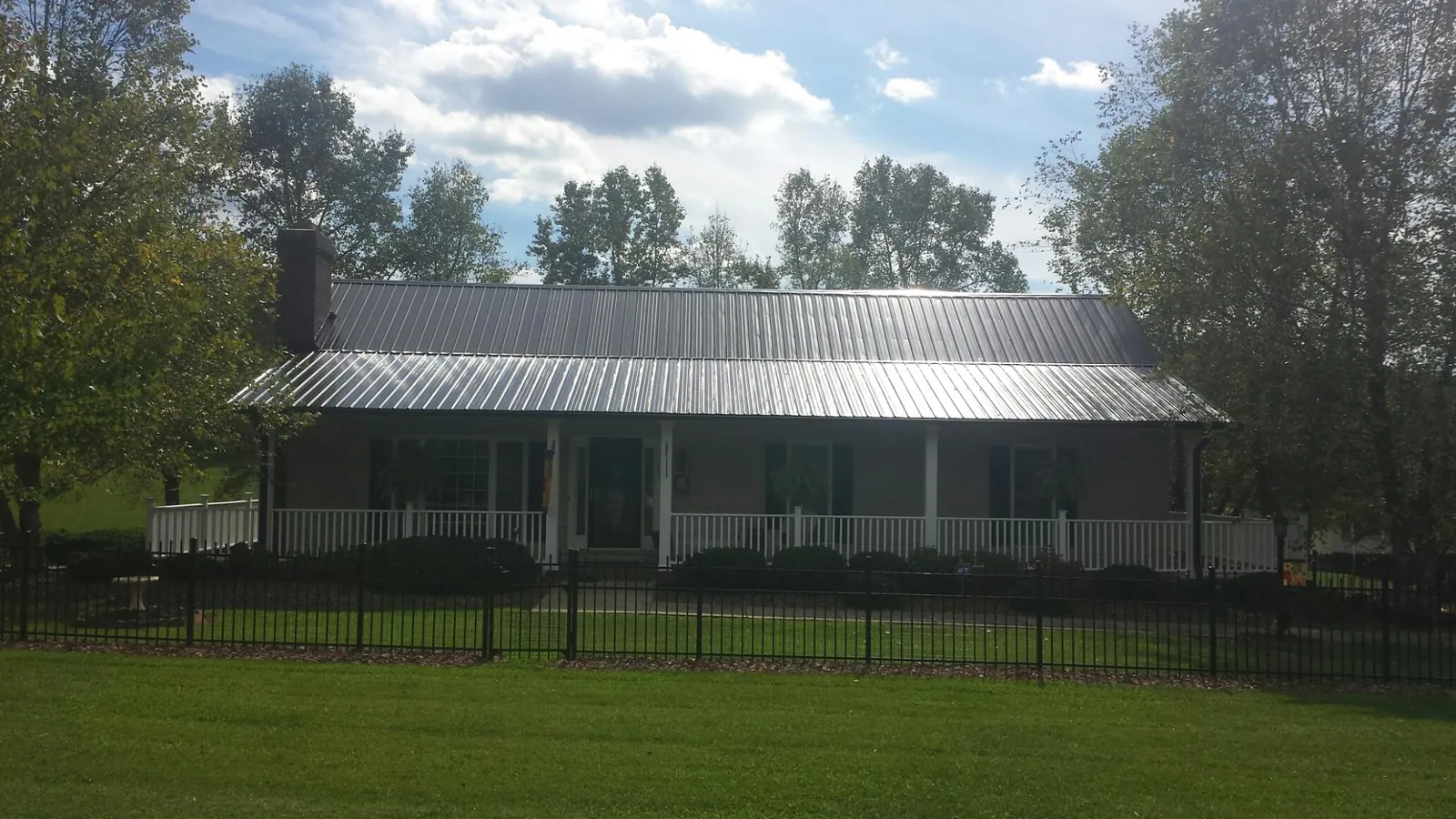 Gray metal roof on a brick ranch with a full width front porch — Gutter Guard Installation work by our crew in Ovid