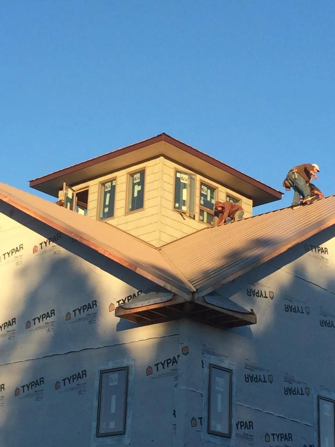 Roofers working around a rooftop cupola on a new metal roof at sunset — Roof Waterproofing in Ovid by Roofing Brothers